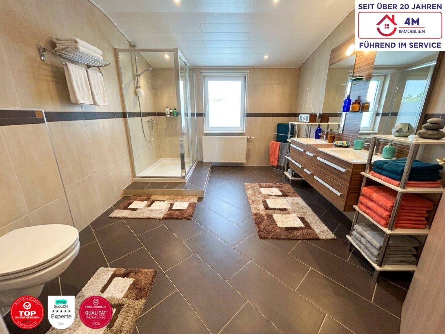 Modernes Badezimmer mit dunklen Fliesen, Doppelwaschbecken und großer Duschkabine.
