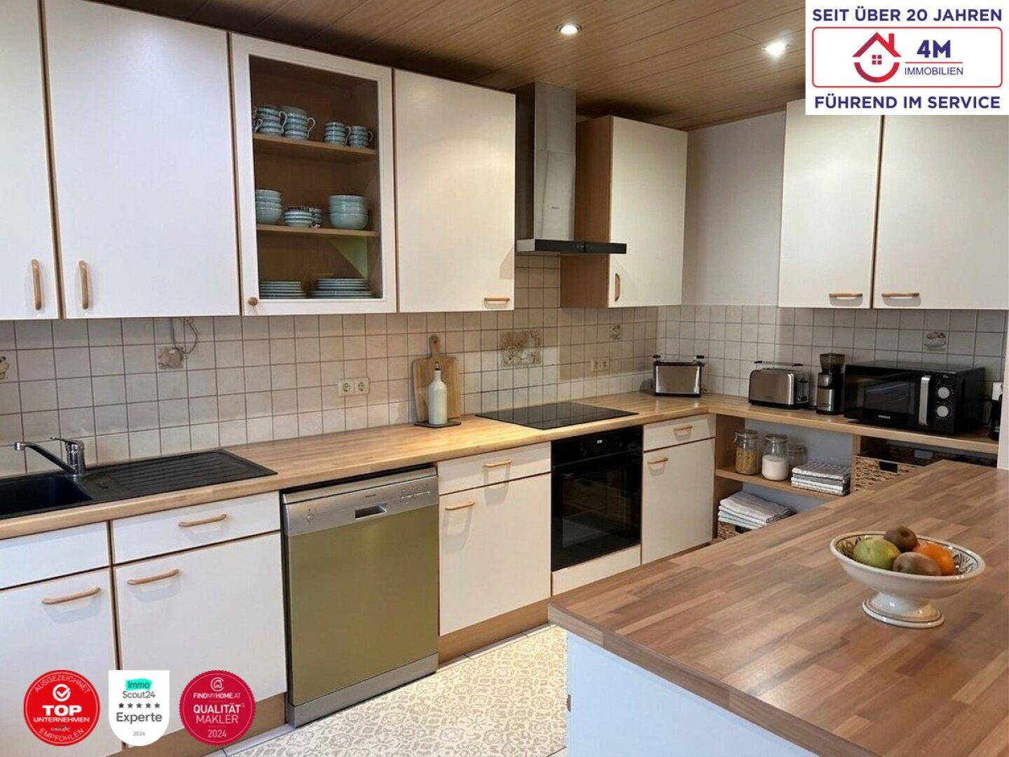 Helle Einbauküche mit weißen Schränken, Holztheke und modernen Geräten.