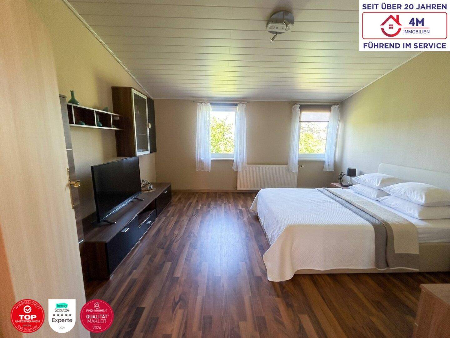 Schlafzimmer mit Laminatboden, Doppelbett und zwei Fenstern für viel Tageslicht.