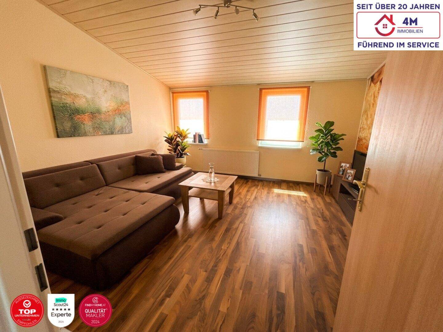 Gemütliches Wohnzimmer mit Laminatboden, bequemer Couch und hellen Fenstern.