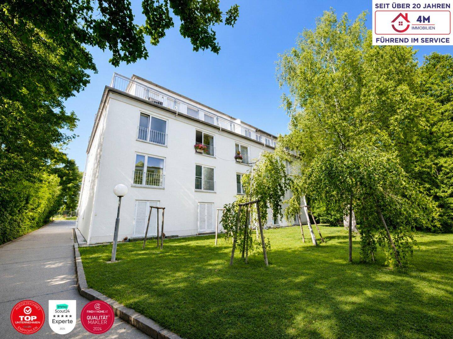 Moderne Wohnanlage mit weißer Fassade, umgeben von einem gepflegten Garten und Bäumen.