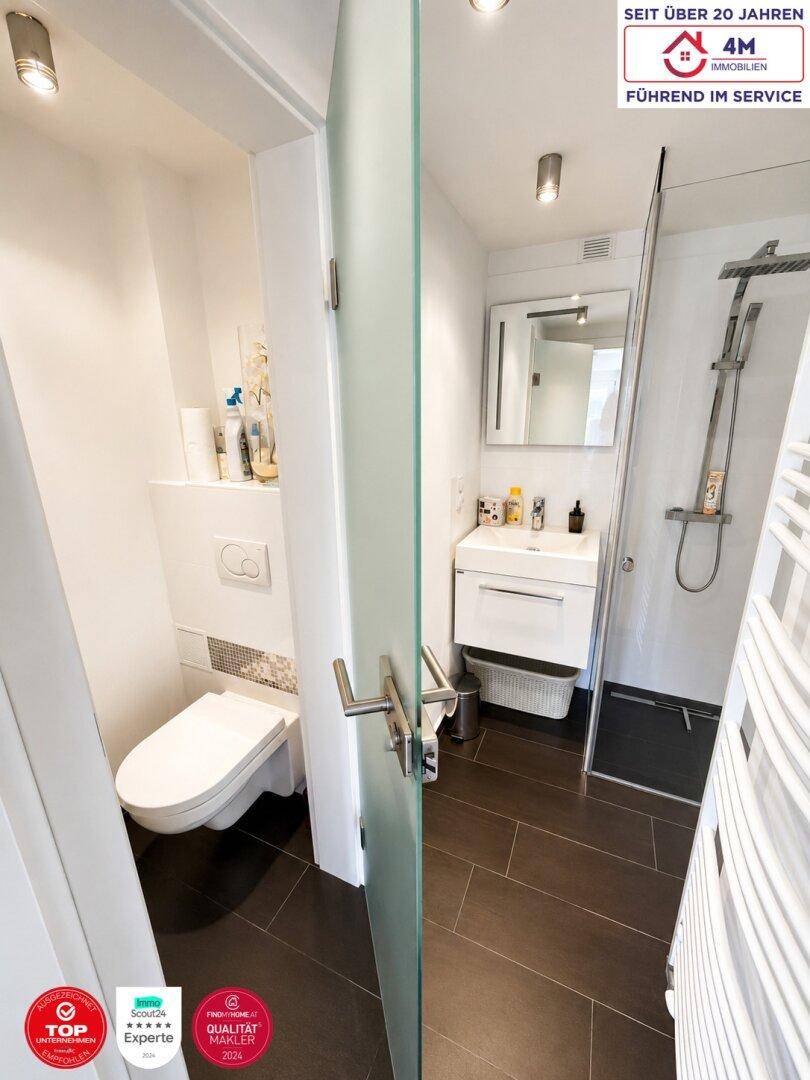Modernes Badezimmer mit dunklen Fliesen, wandhängendem WC und Glasdusche.