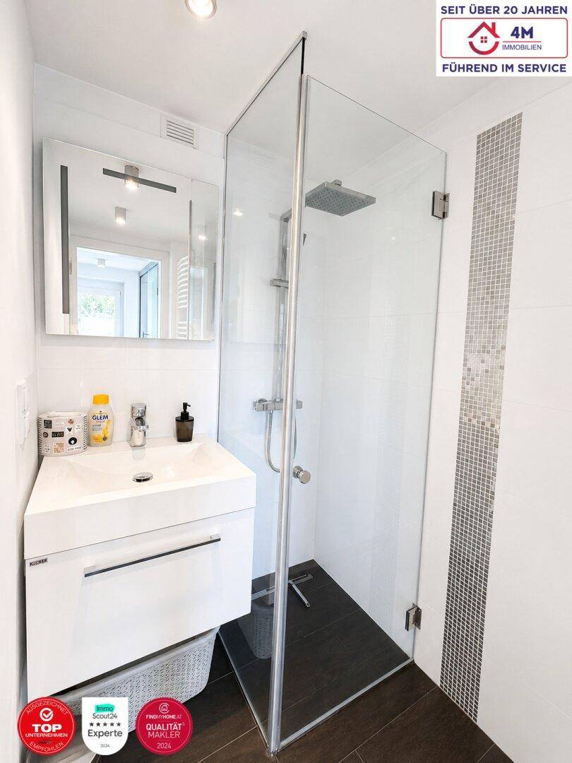 Helles Badezimmer mit moderner Glasdusche, Einzelwaschbecken und dunklem Fliesenboden.