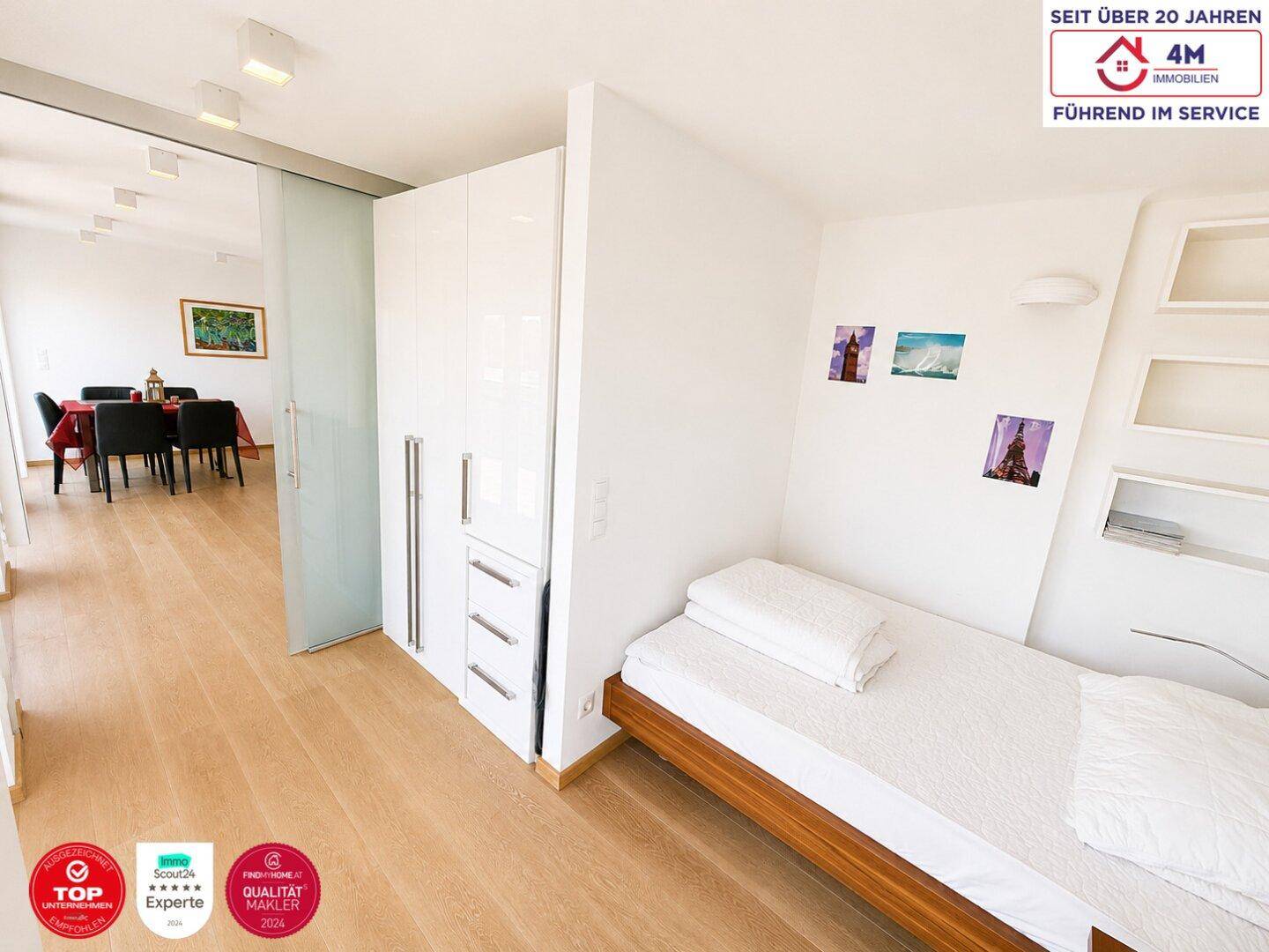 Helles Schlafzimmer mit Holzboden und weißem Kleiderschrank, verbunden mit dem Wohnbereich durch eine Glasschiebetür.