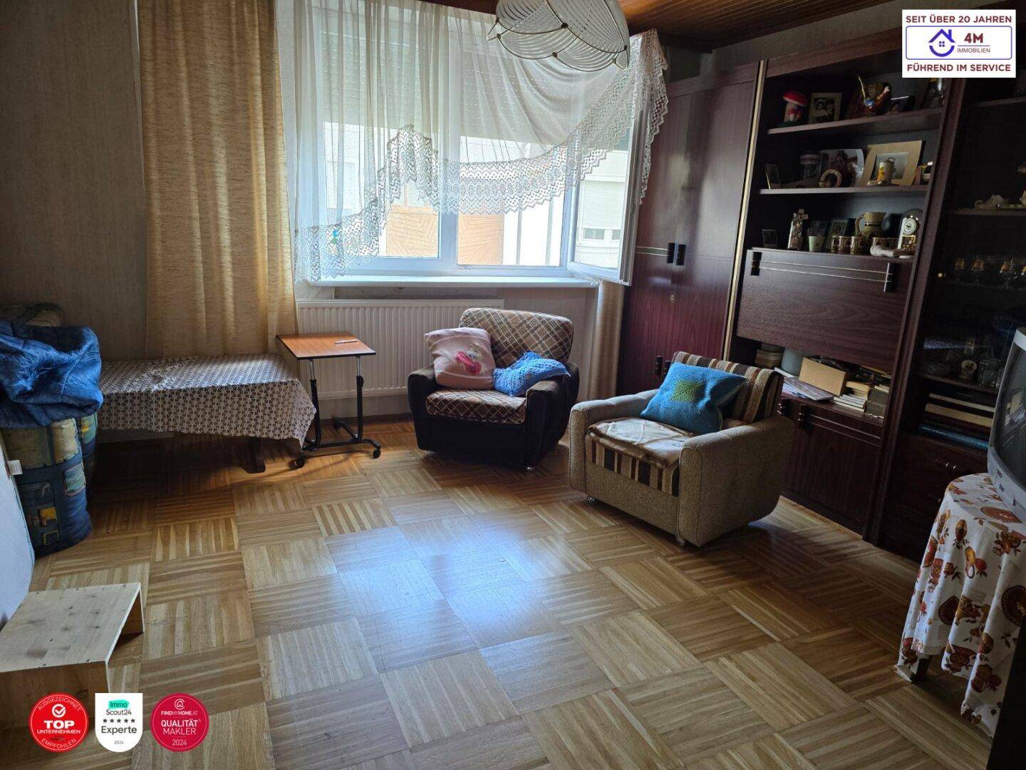 Wohnzimmer mit Parkettboden, Holzdecke und einem großen Fenster mit Vorhängen.