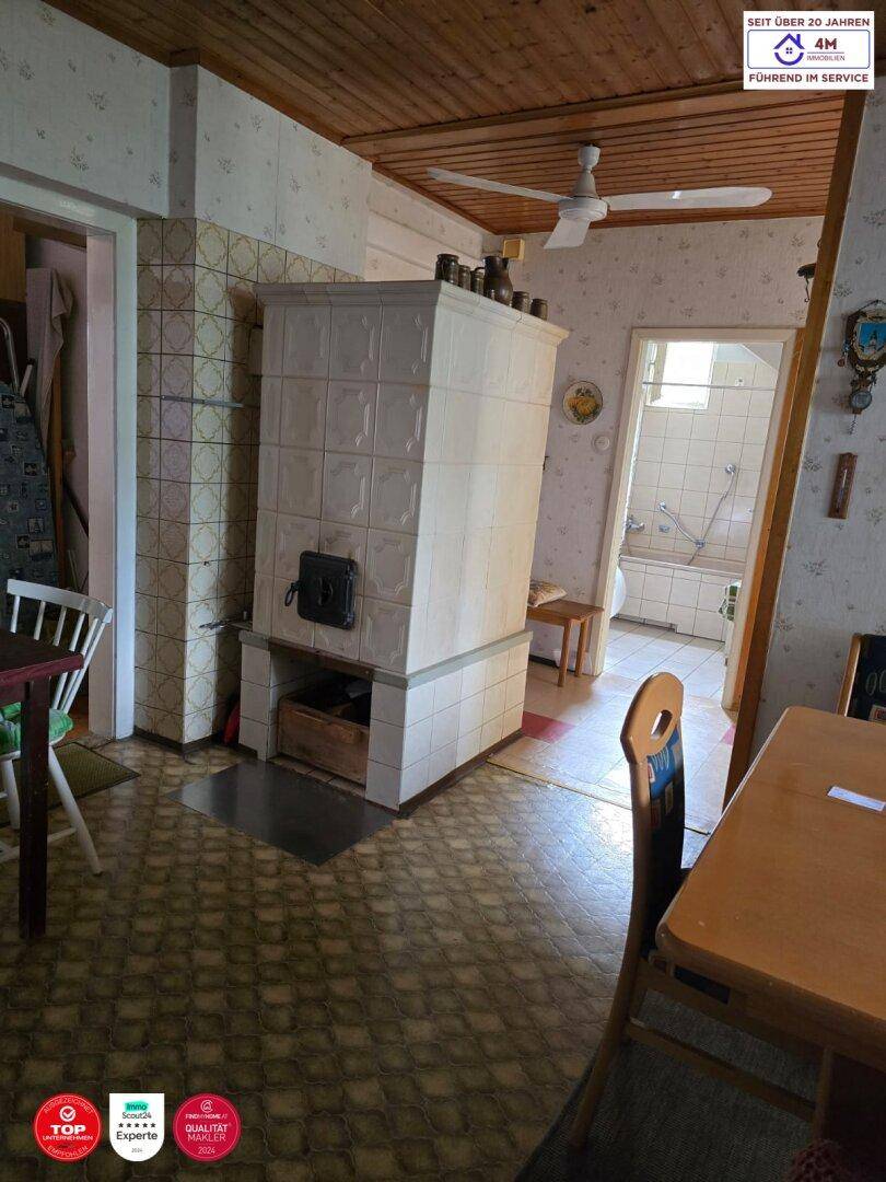 Gemütlicher Innenraum mit einem traditionellen Kachelofen, Holzdecke und Deckenventilator.