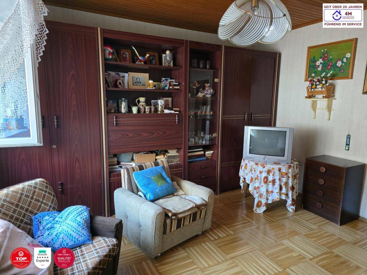 Wohnzimmer mit Holzschrankwand, Parkettboden und einem Fernseher, der eine gemütliche Atmosphäre schafft.