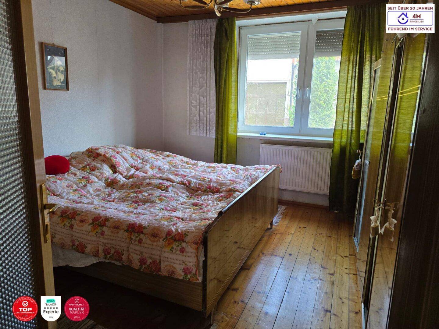 Schlafzimmer mit Holzboden, einem Doppelbett und einem Fenster mit grünen Vorhängen.