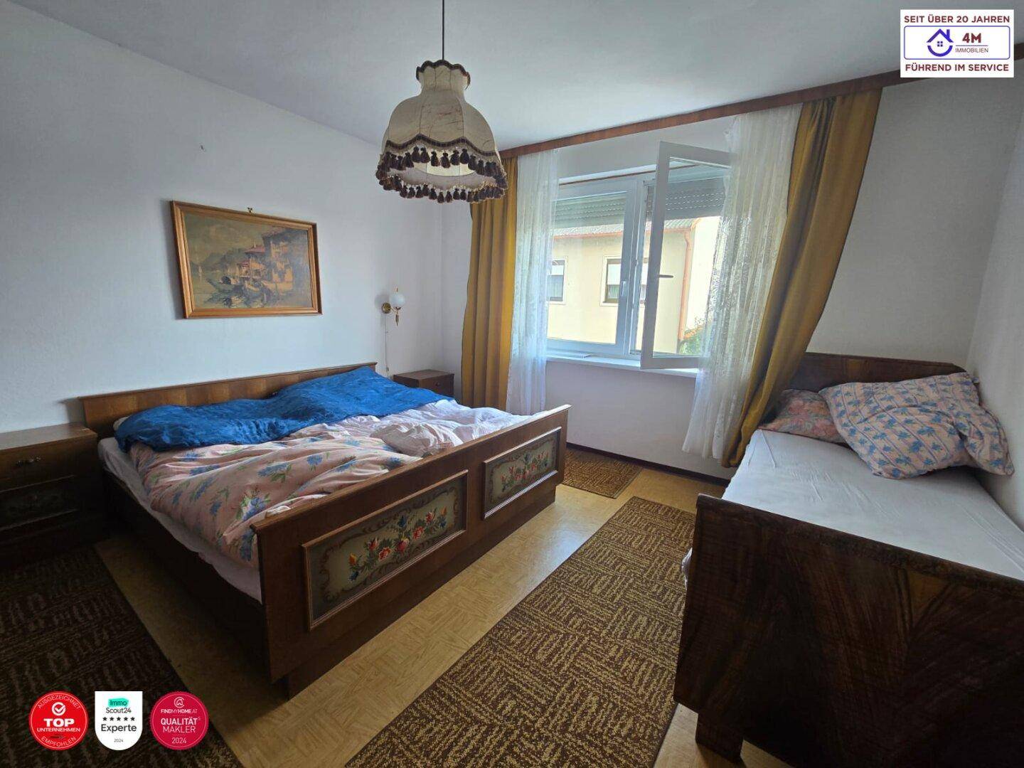 Schlafzimmer mit Holzbett, Teppichläufern und einem Fenster, das viel Tageslicht hereinlässt.