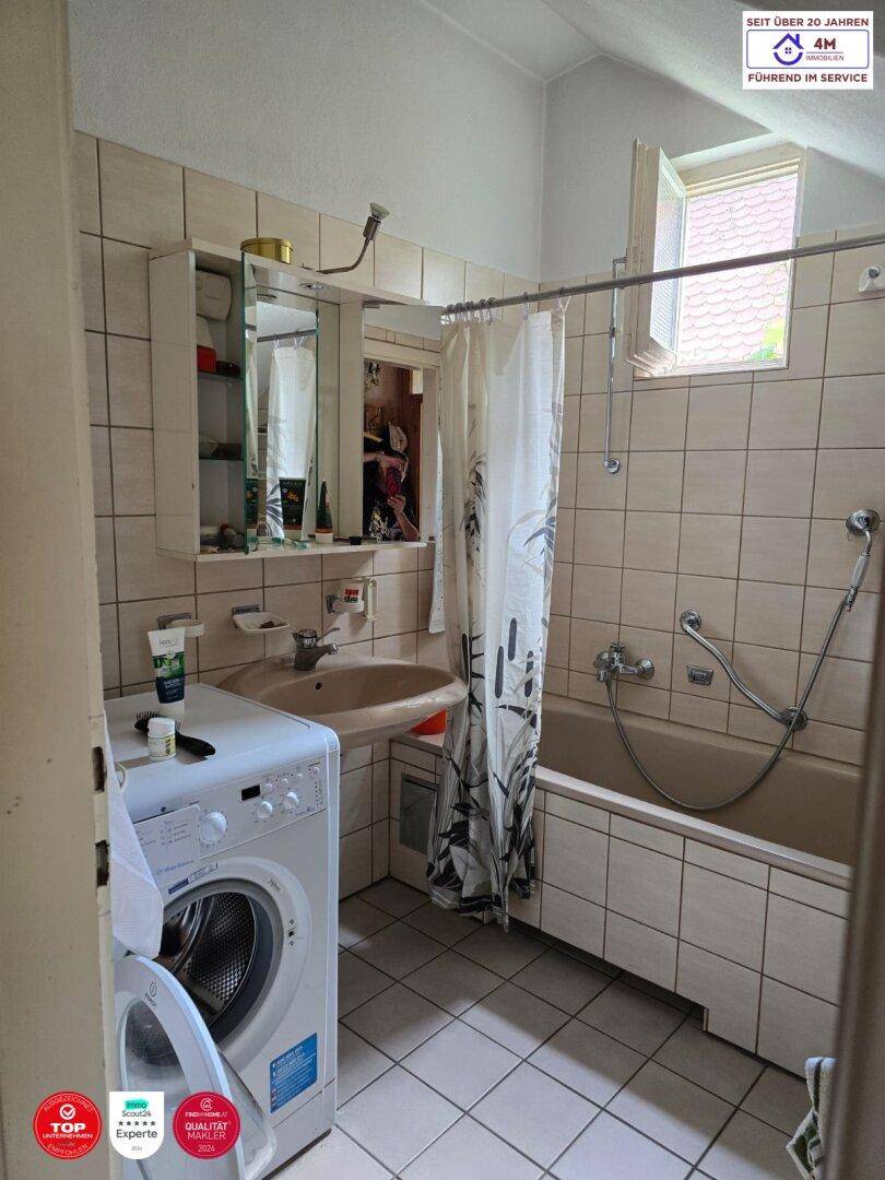Badezimmer mit Badewanne, Waschmaschine und einem Fenster, das für Belüftung sorgt.