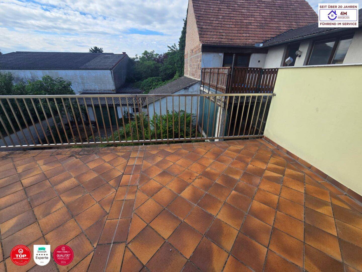 Große geflieste Terrasse mit Metallgeländer und Blick auf die umliegenden Dächer.