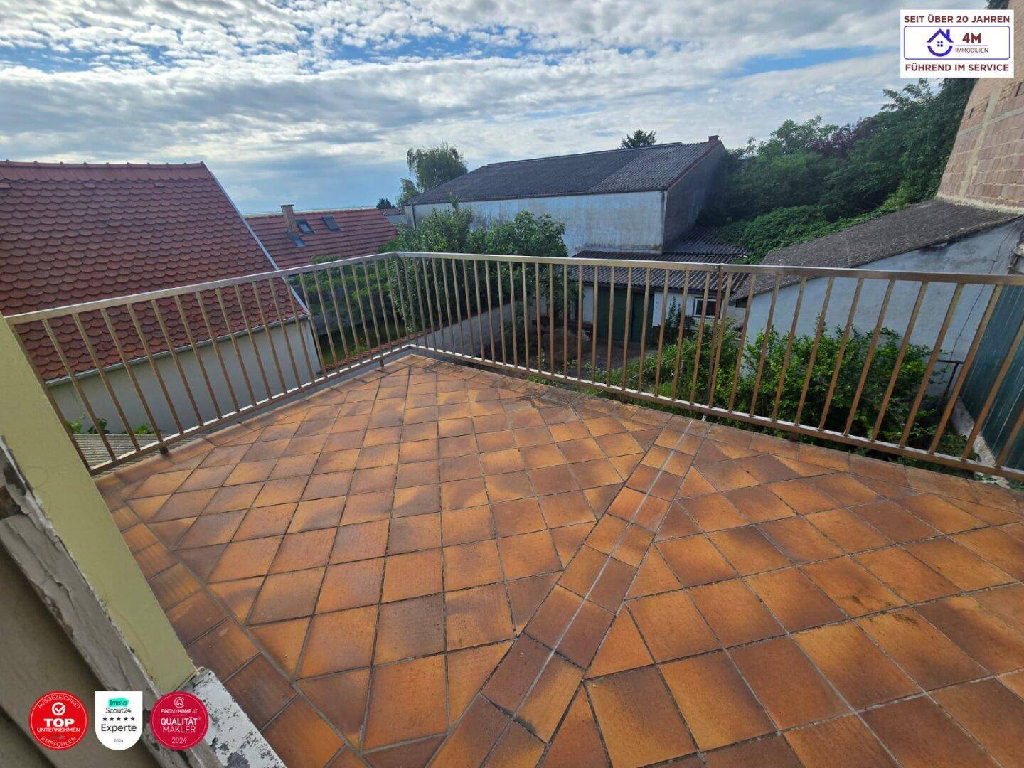 Weitläufige Terrasse mit Terrakottafliesen und einem stabilen Metallgeländer unter blauem Himmel.