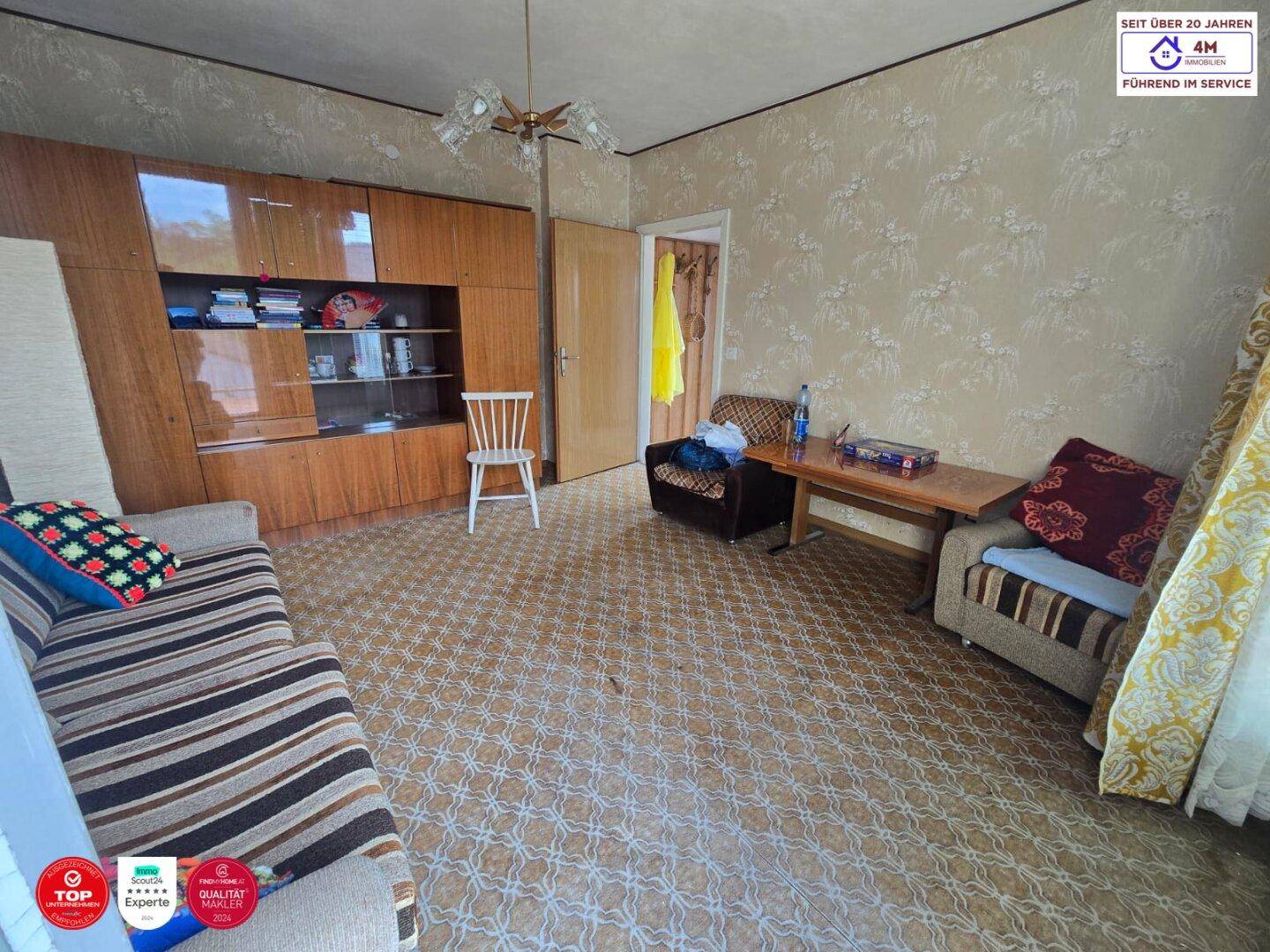 Wohnzimmer mit gemustertem Boden, Holzschrank und einem Sofa mit gestreiften Kissen.