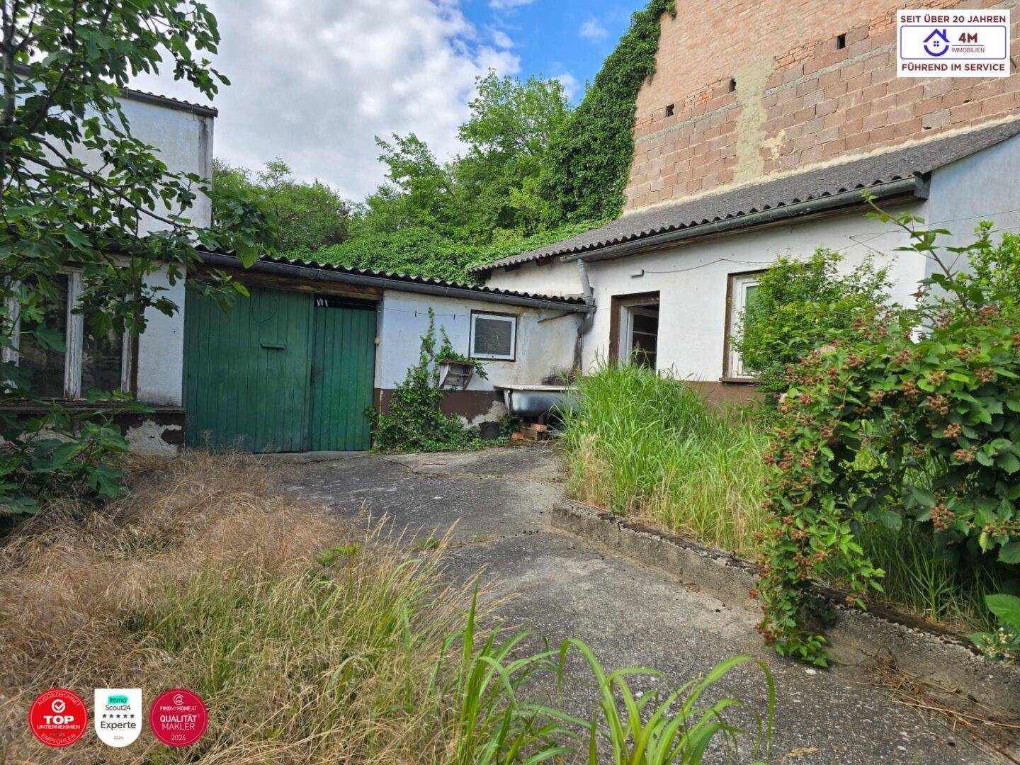Hinterhof mit Nebengebäuden, viel Grün und einem unbefestigten Weg.
