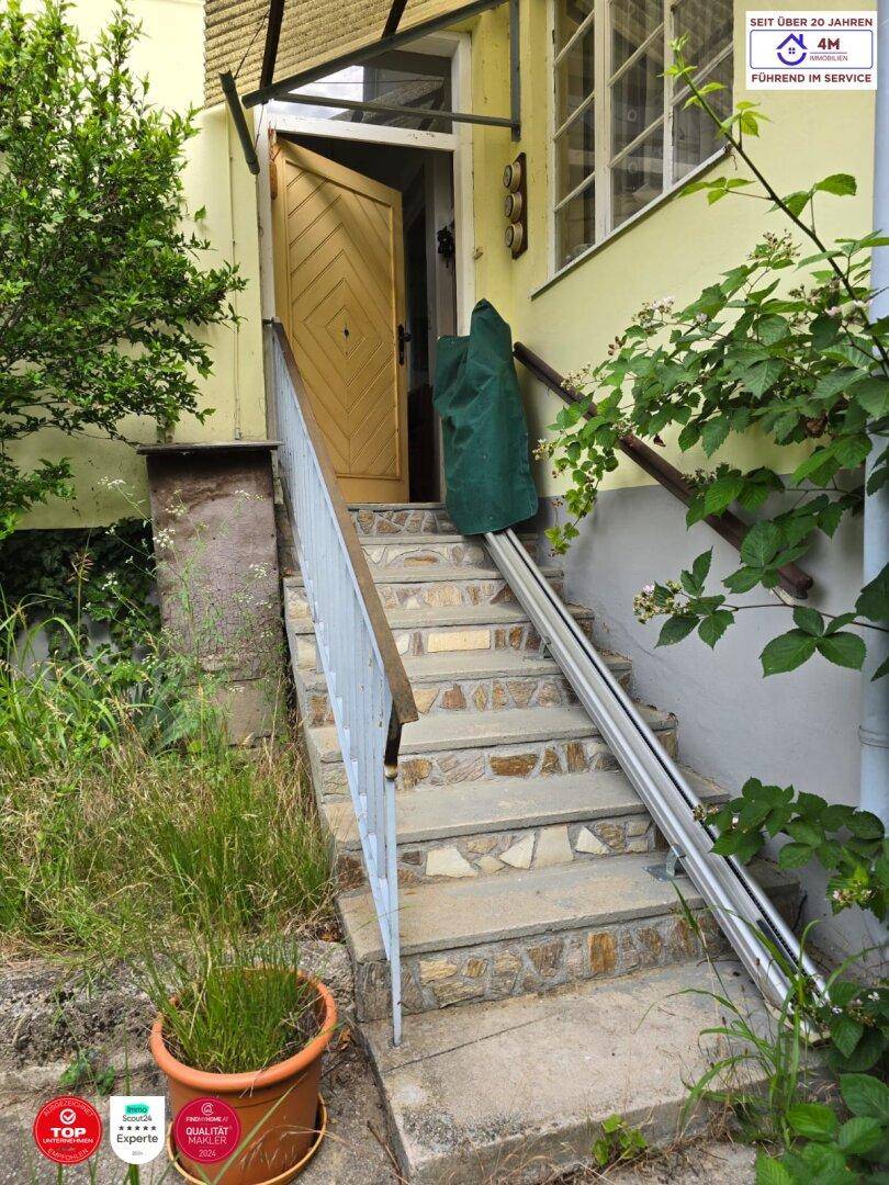 Eingangsbereich mit Steintreppe und einem Treppenlift für barrierefreien Zugang.
