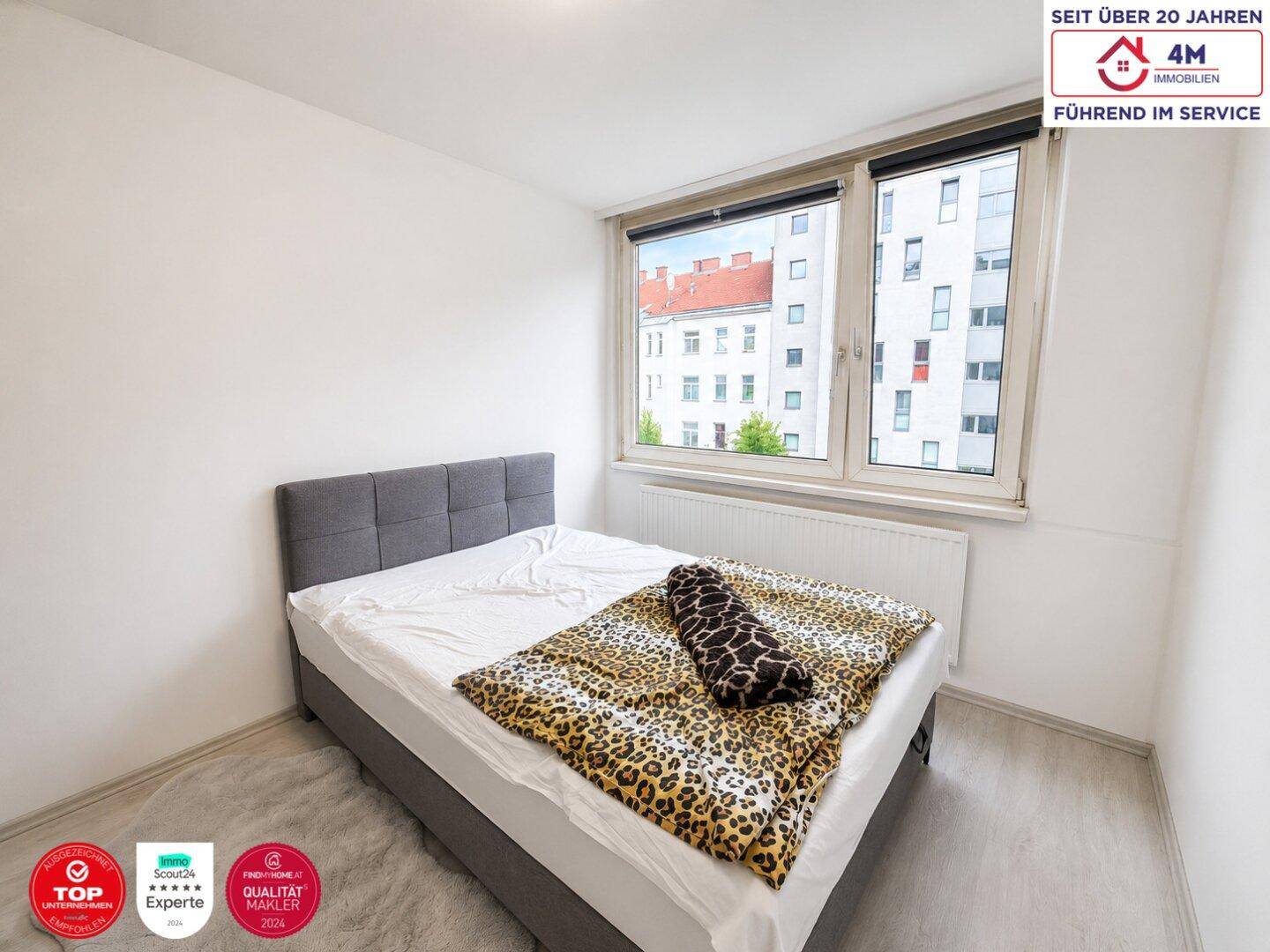 Helles Schlafzimmer mit Doppelbett, Laminatboden und großem Fenster für viel Tageslicht und frische Luft.