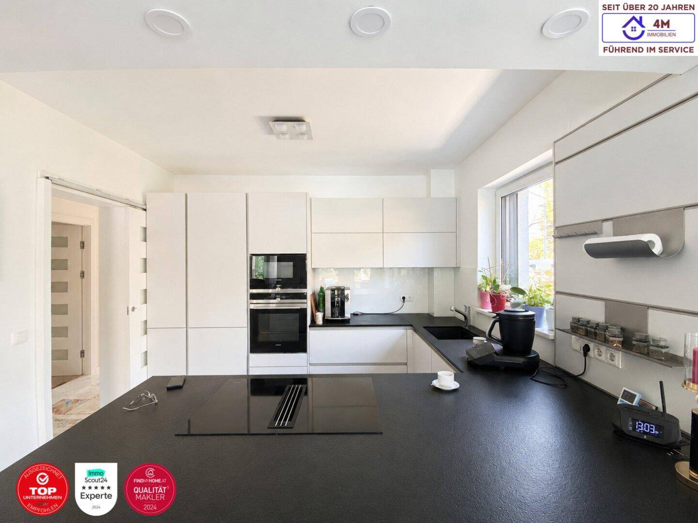 Moderne weiße Küche mit schwarzen Arbeitsplatten, integrierten Geräten und viel Stauraum.
