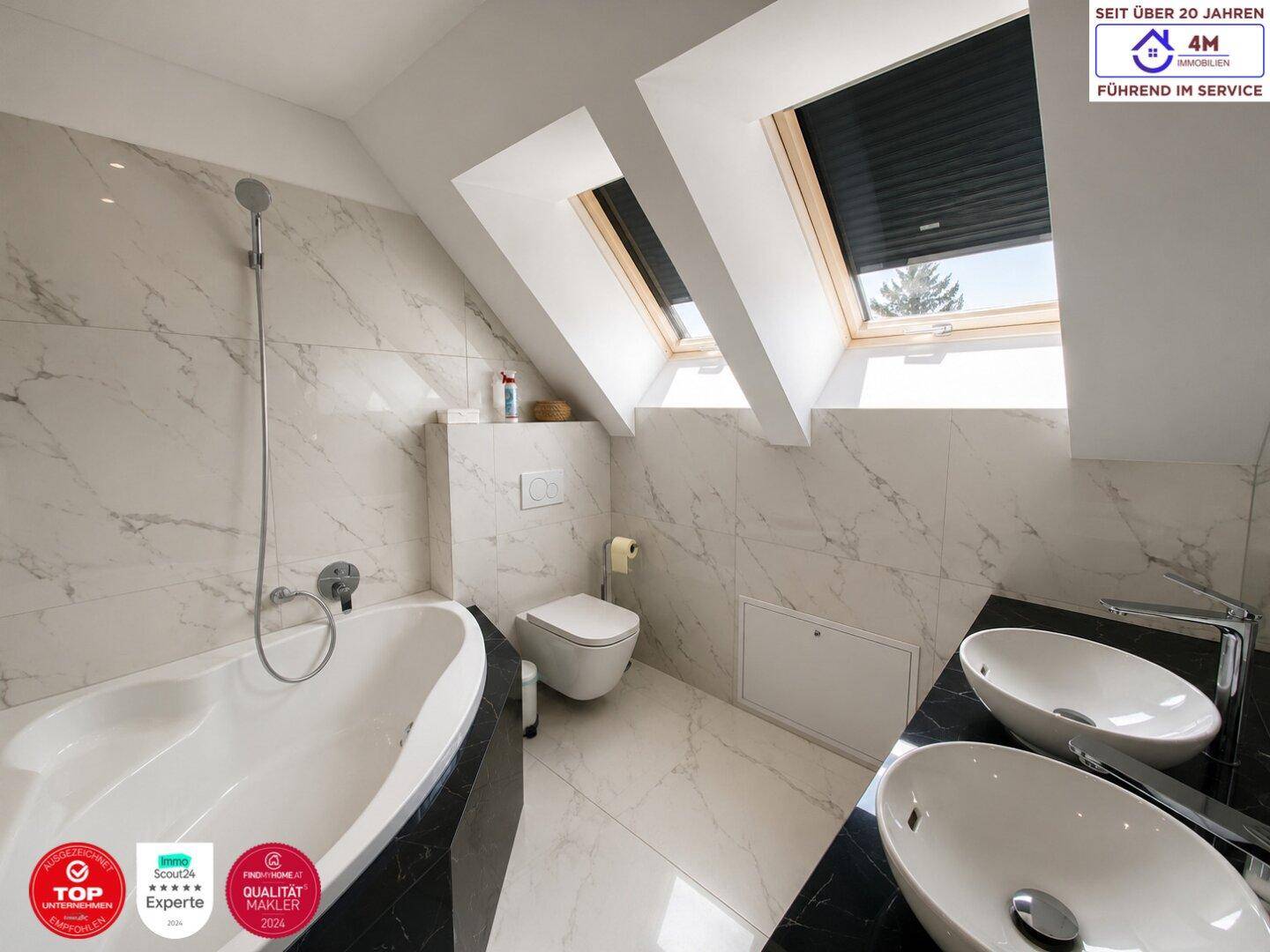 Modernes Badezimmer im Dachgeschoss mit Badewanne, Doppelwaschbecken und Marmorfliesen.