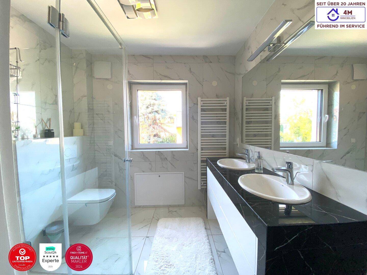 Elegantes Badezimmer mit Doppelwaschbecken, großer Spiegelfläche und Marmorfliesen.