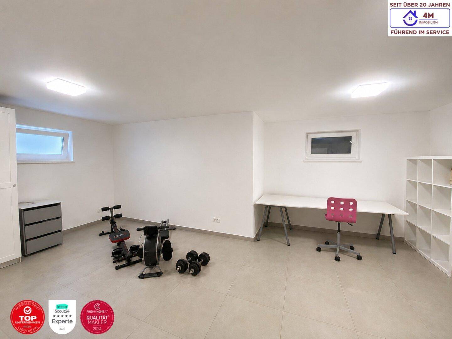 Großer Raum, eingerichtet als Fitnessbereich mit Sportgeräten und Schreibtisch.