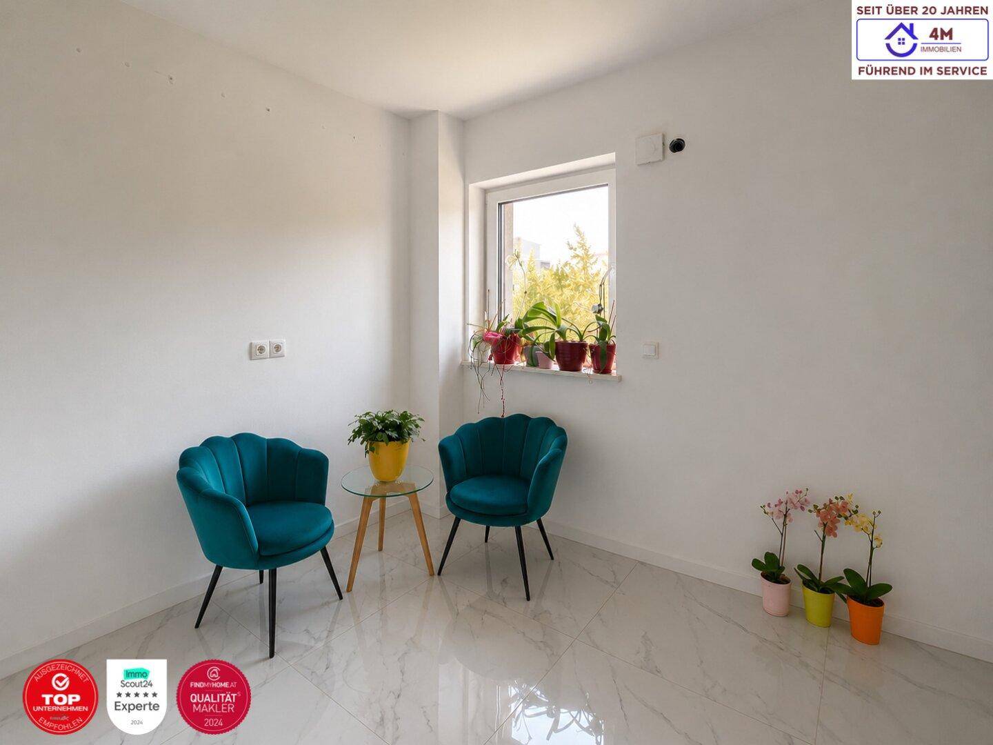 Helles Zimmer mit modernen türkisfarbenen Sesseln, weißem Marmorboden und einem Fenster mit Pflanzen.