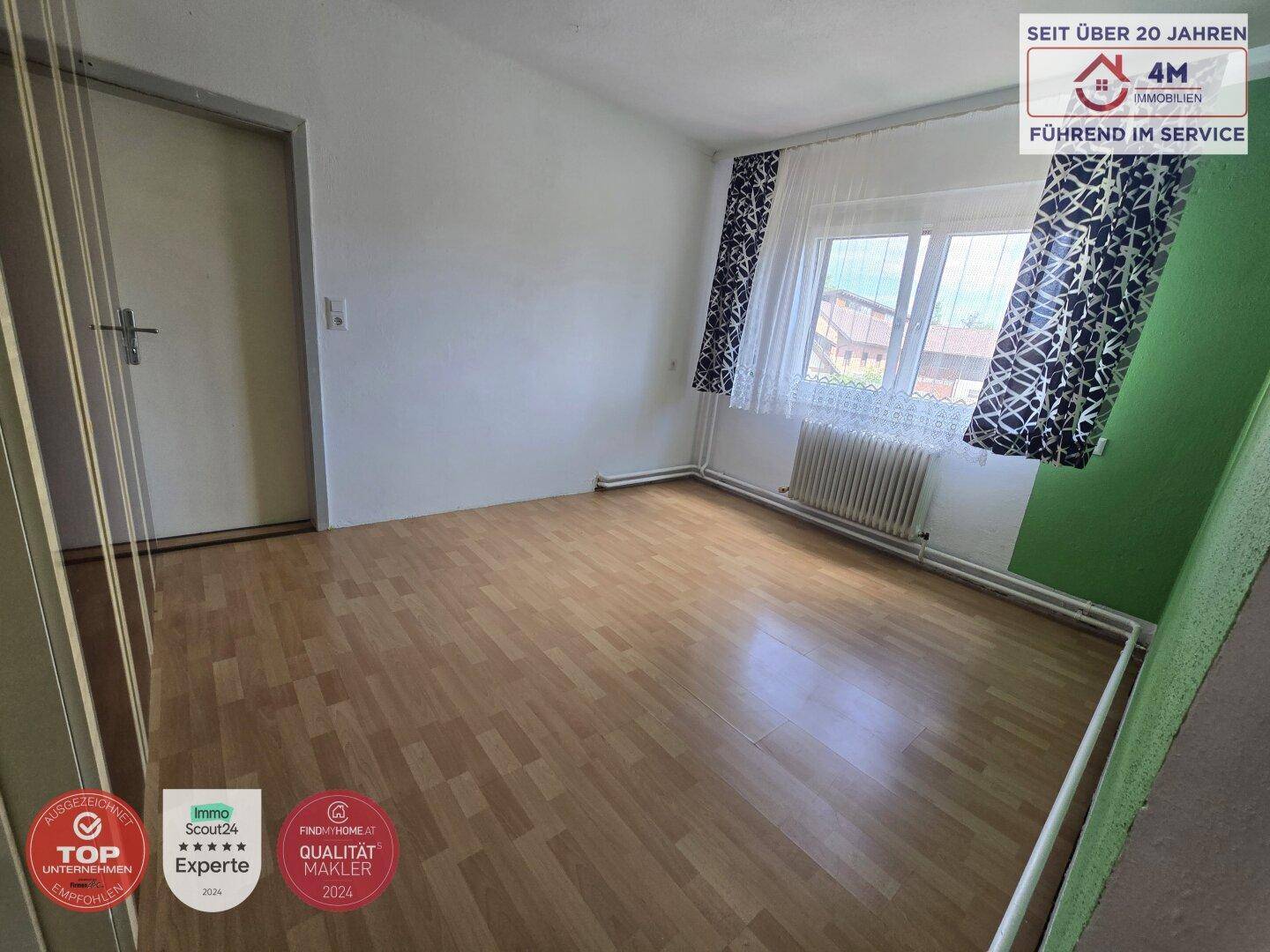 Leeres Zimmer mit Laminatboden, Fenster und Heizkörper, bereit zur individuellen Gestaltung.
