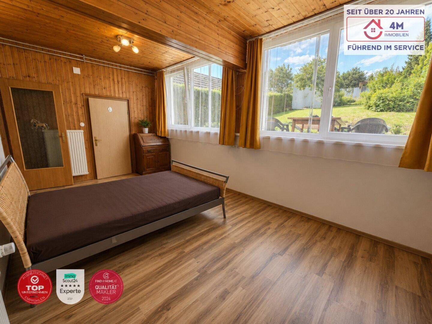 Gemütliches Schlafzimmer mit Holzdecke, Laminatboden und Blick in den Garten.