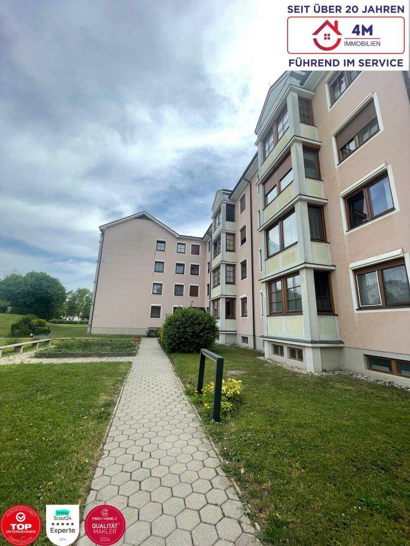 Außenansicht des Mehrfamilienhauses mit gepflegter Grünfläche und Gehwegen.