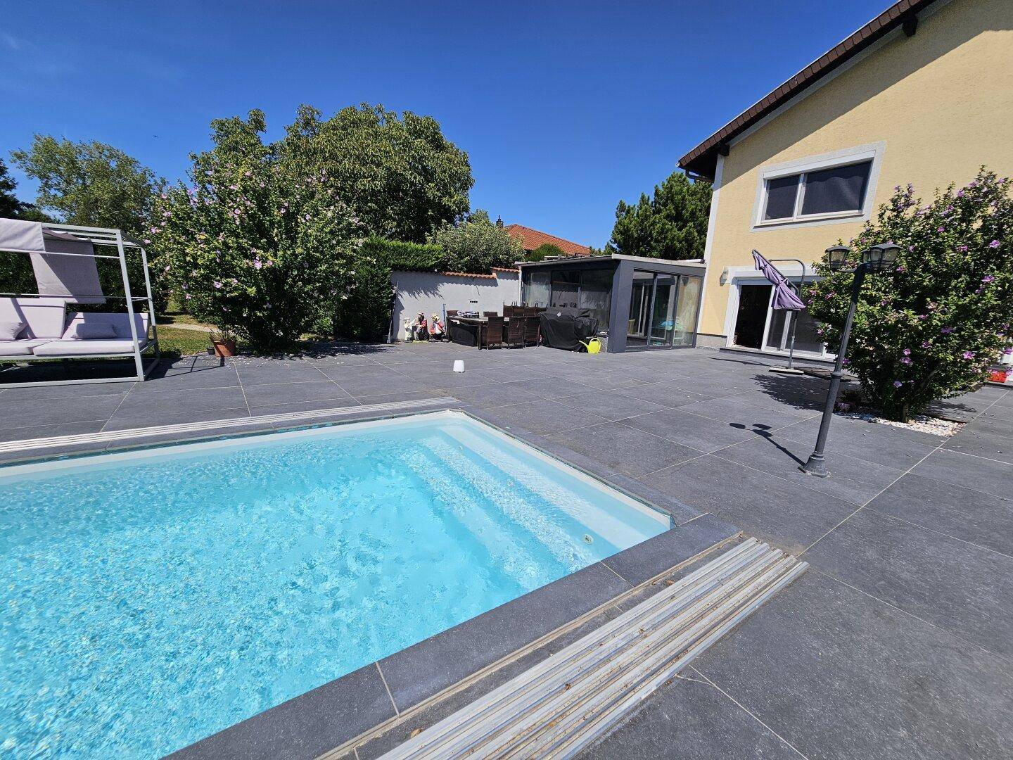 Großer Gartenbereich mit Swimmingpool, gepflasterter Terrasse und gemütlicher Outdoor-Lounge.