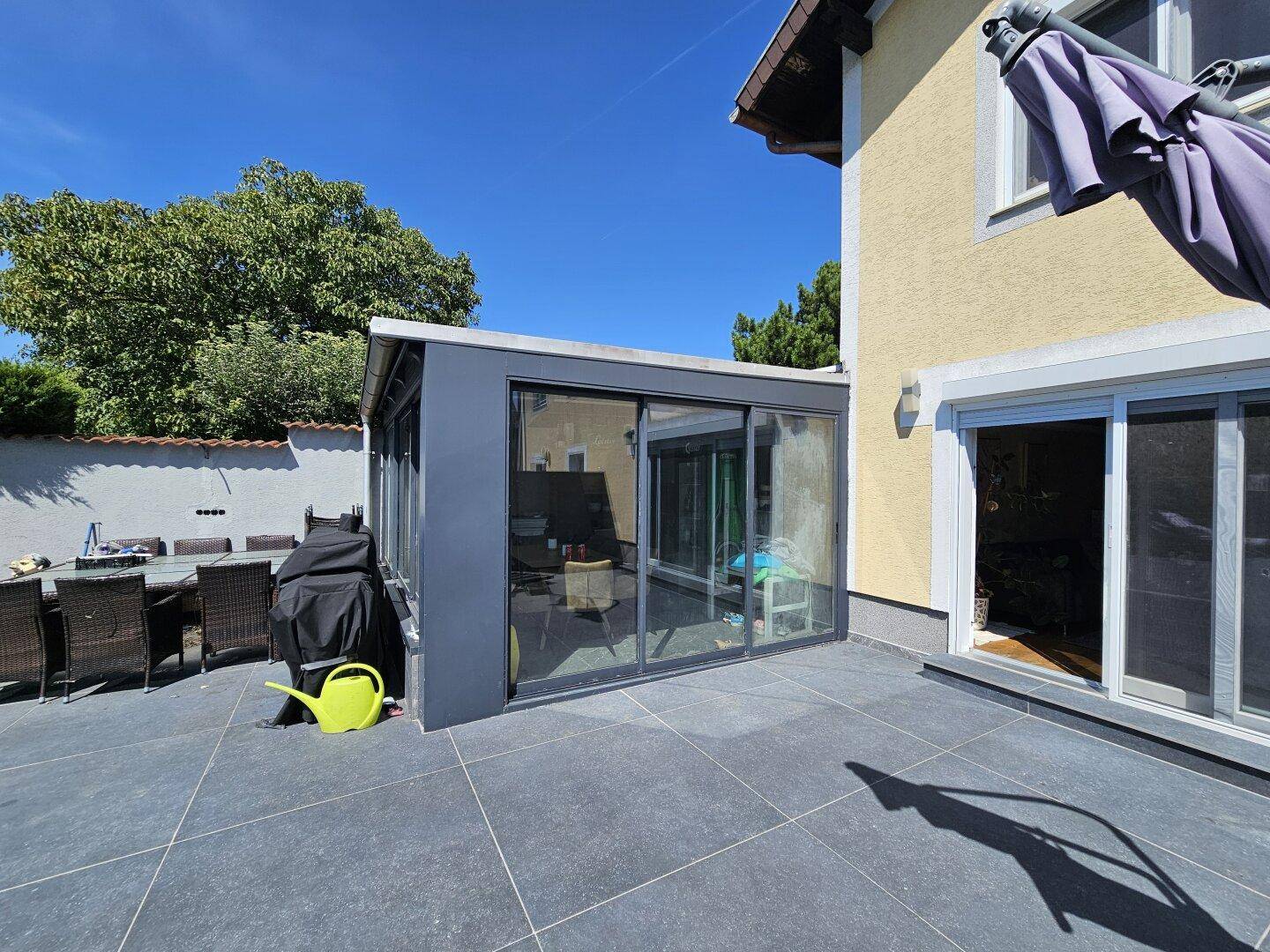 Überdachte Terrasse mit Essbereich und angrenzendem Wintergarten am Haus.