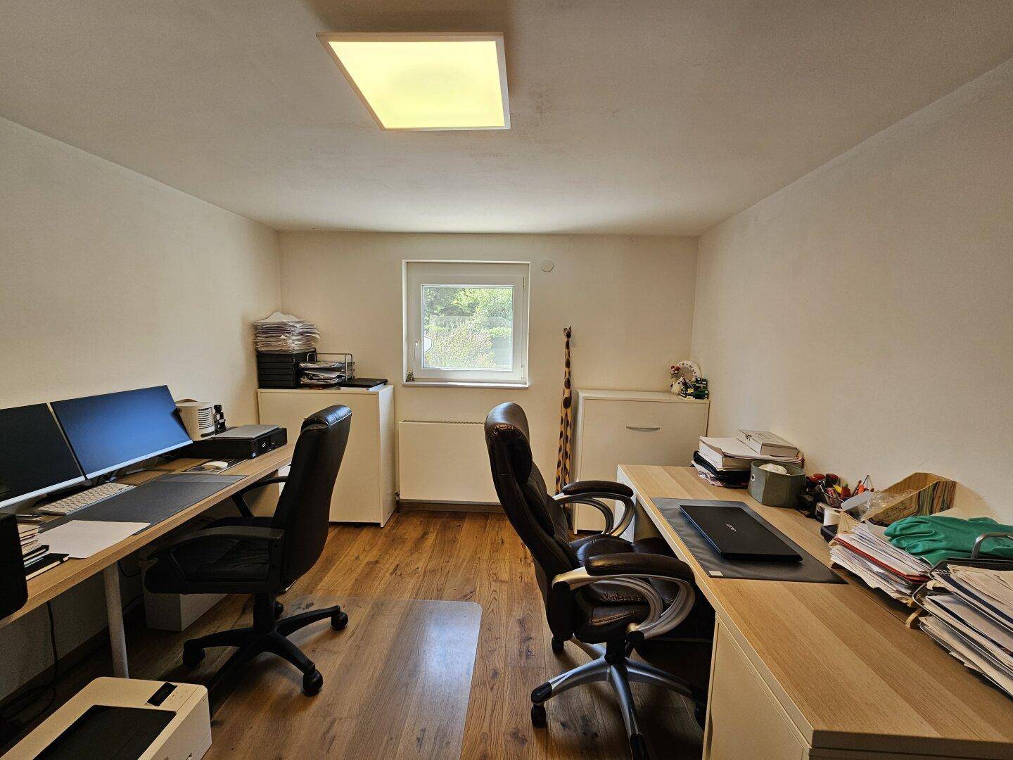 Funktionales Büro mit zwei Arbeitsplätzen, Holzfußboden und natürlichem Lichteinfall.