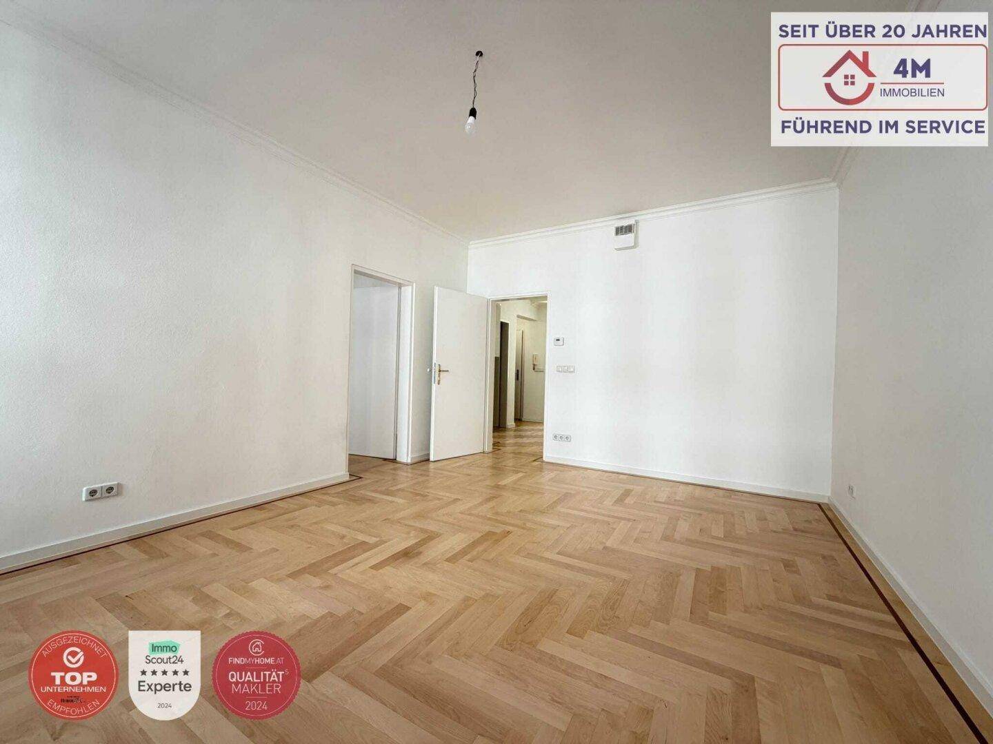Geräumiges Zimmer mit hellem Fischgrätparkett und Zugang zu weiteren Räumen.