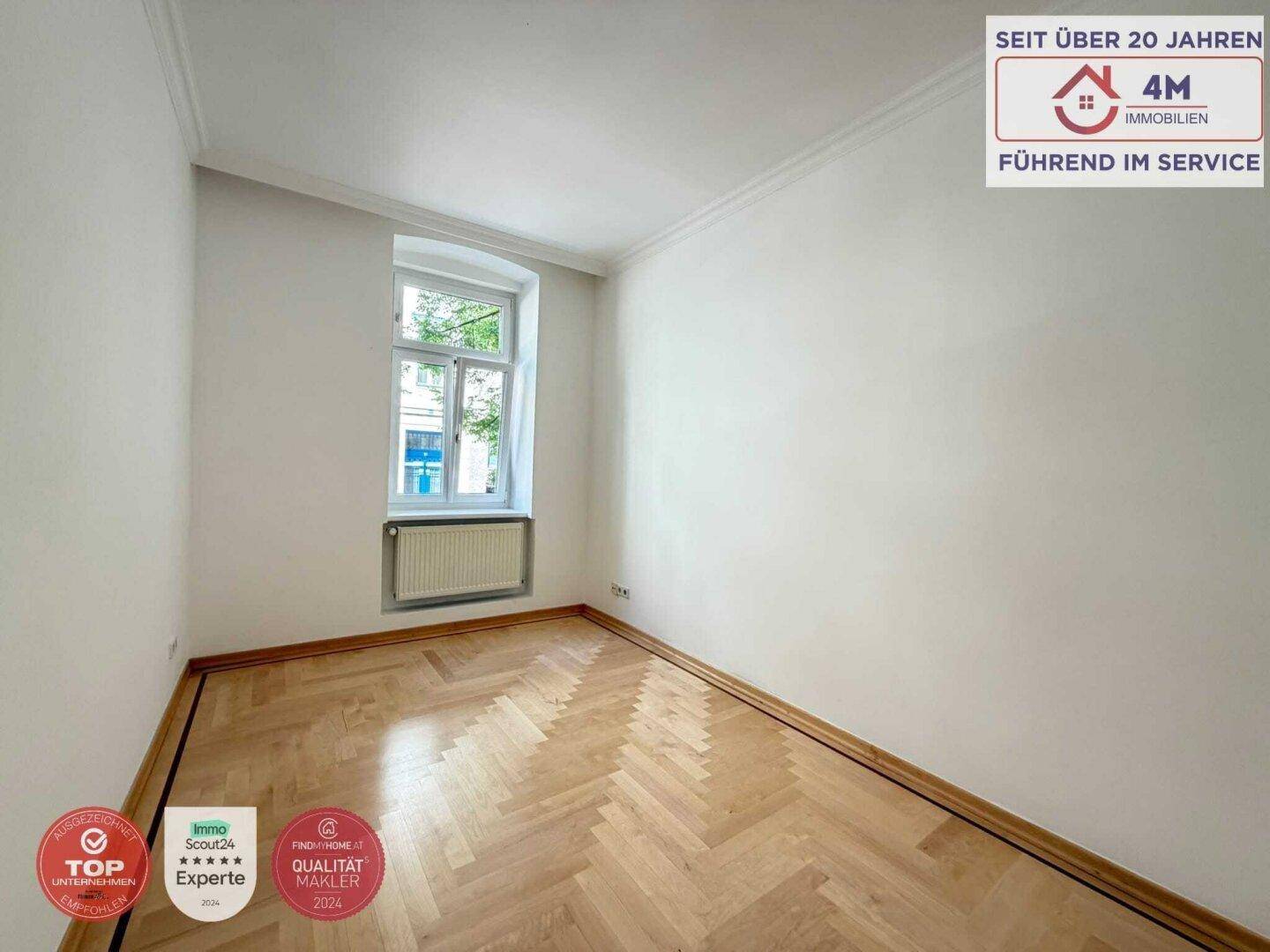 Helles Schlafzimmer mit Fischgrätparkett und einem Fenster, das viel Tageslicht hereinlässt.