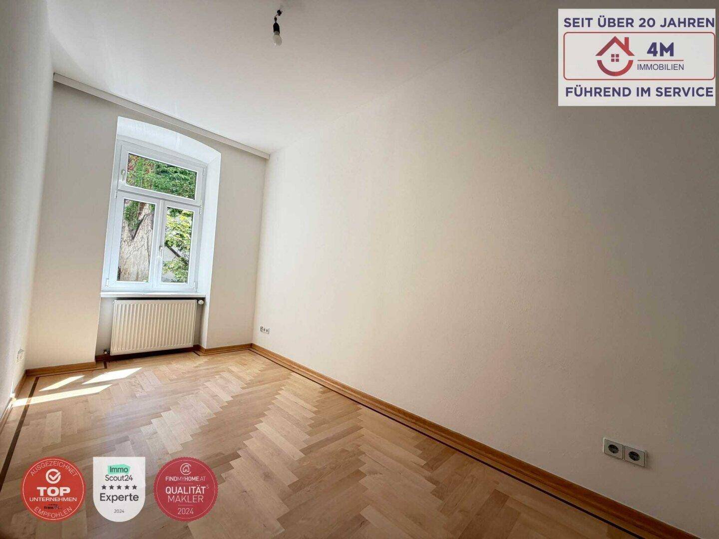 Ruhiges Zimmer mit Fischgrätparkett und einem Fenster mit Blick ins Grüne.