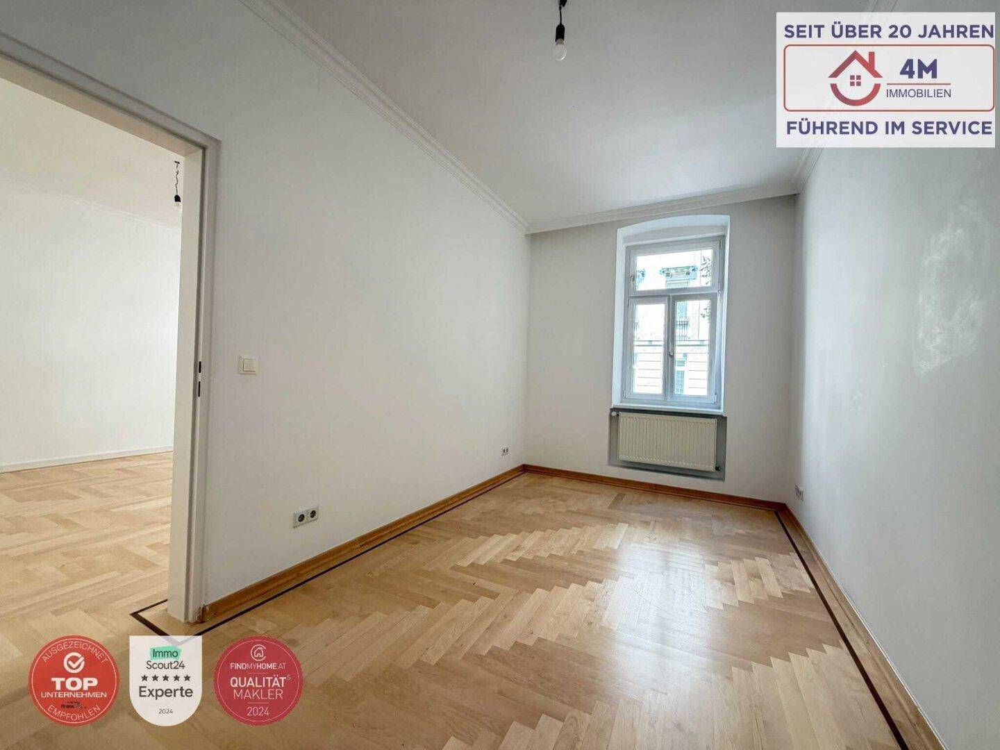 Helles Zimmer mit Fischgrätparkett und offenem Zugang zu einem weiteren Raum.