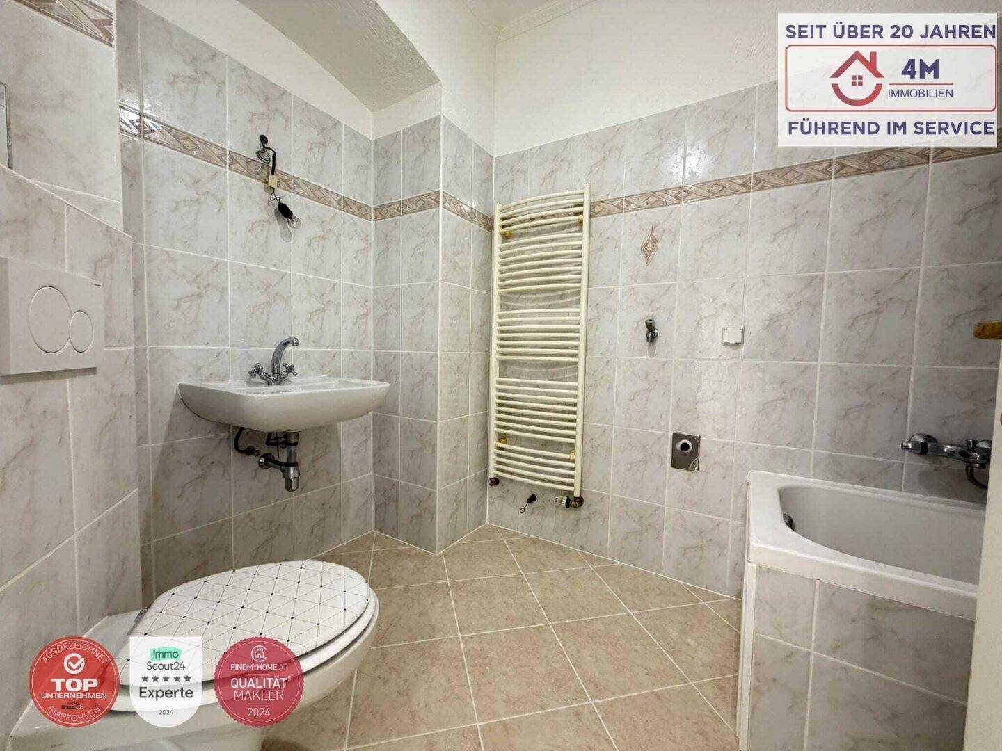 Gefliestes Badezimmer mit Badewanne, WC, Waschbecken und Handtuchheizkörper.