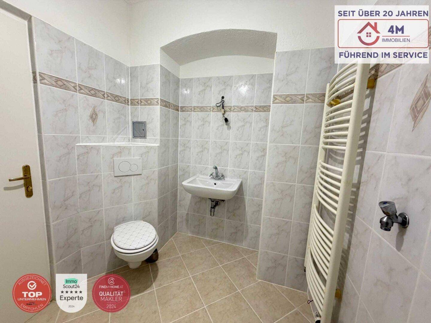 Badezimmer mit WC, Waschbecken und Fliesen in neutralen Farbtönen.