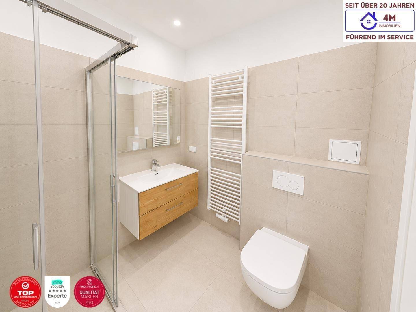 Helles Badezimmer mit Fliesen, einer Duschkabine, einem schwebenden Waschtisch und einem WC.