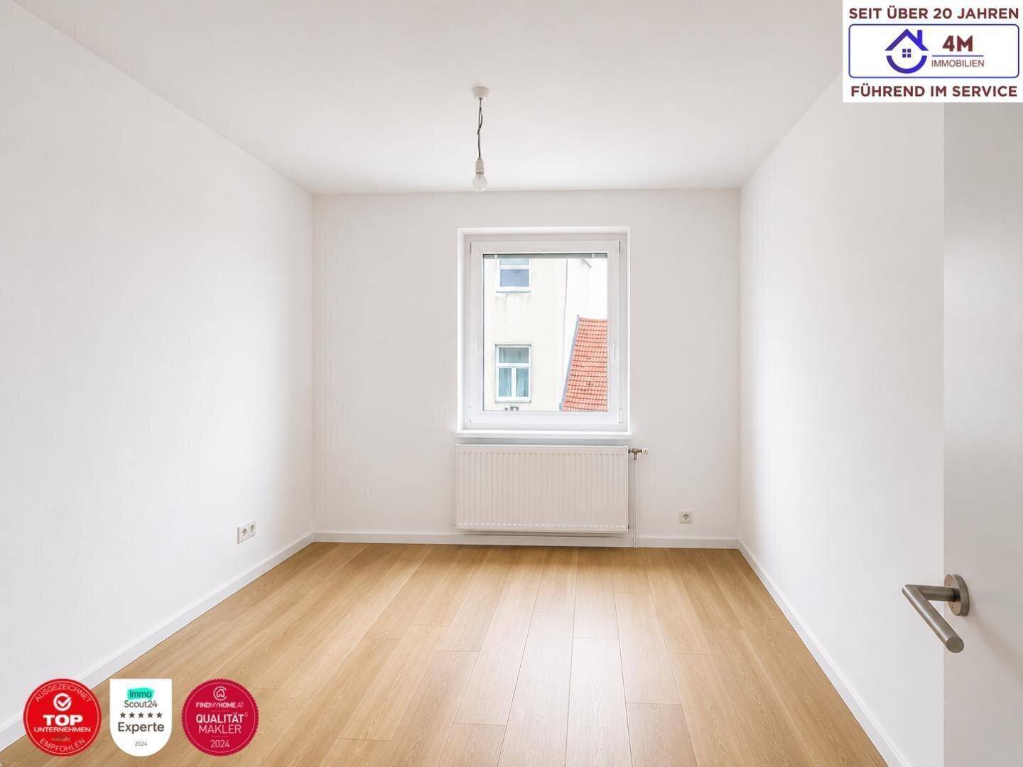 Gemütliches, leeres Zimmer mit Parkettboden und einem Fenster, das einen Blick nach draußen bietet.