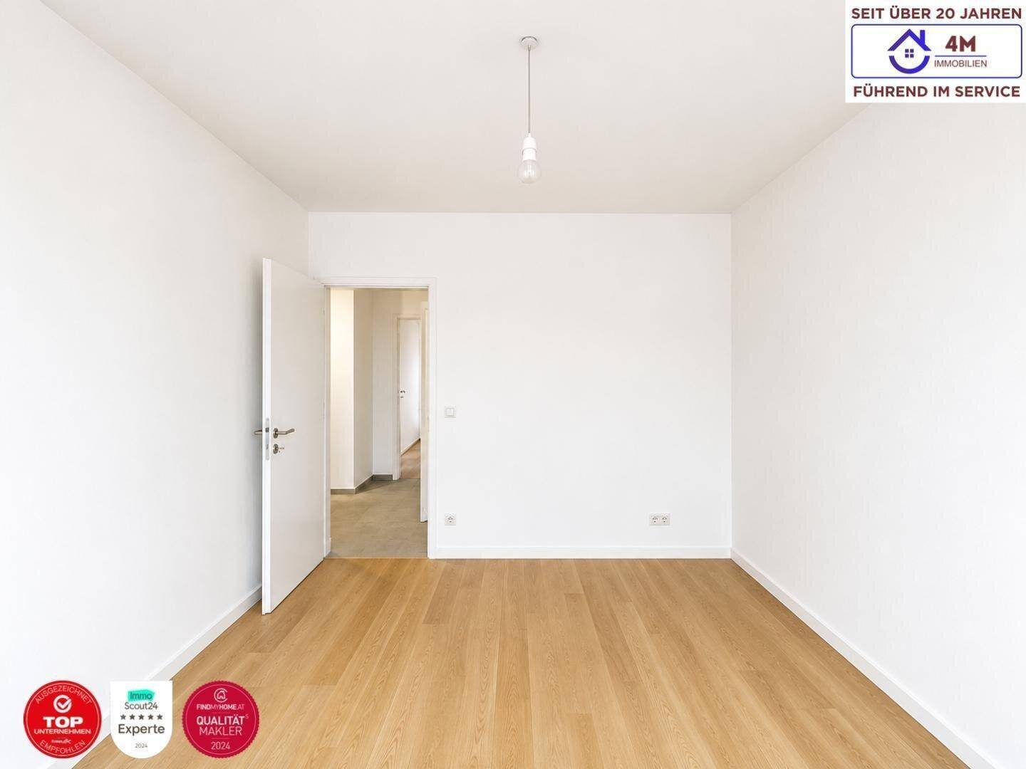 Leeres Zimmer mit hellem Parkettboden und einer offenen Tür, die den Blick in den Flur freigibt.
