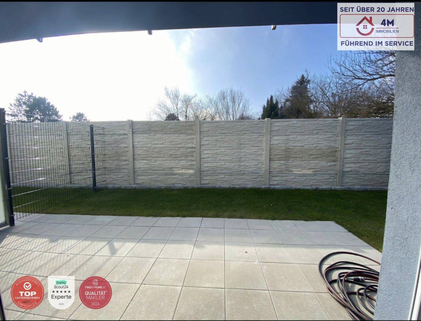 Private Terrasse mit angrenzendem Rasen und einem modernen Sichtschutzzaun im Außenbereich.