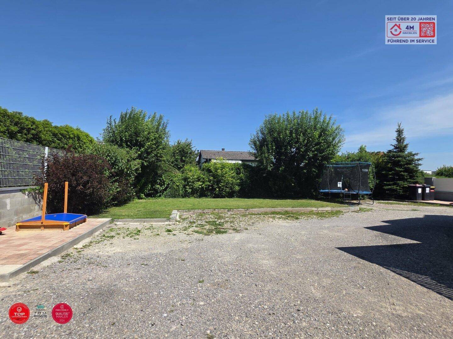 Großer Gartenbereich mit Rasenfläche, Sandkasten, Trampolin und umgebenden Hecken.