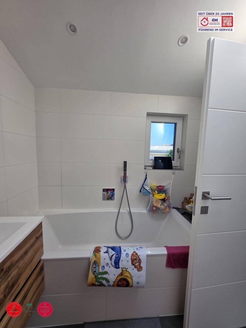Badezimmer mit Badewanne, kleinem Fenster und Holzwaschtisch.