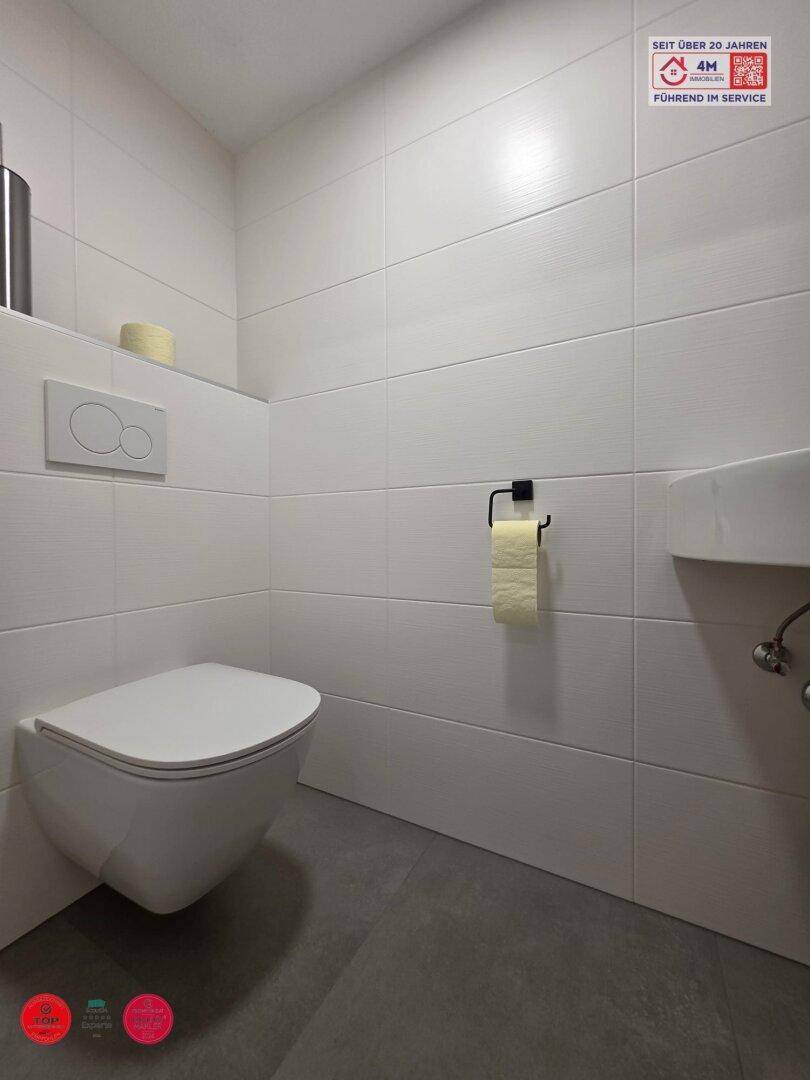 Separates WC mit wandhängender Toilette und kleinem Waschbecken.