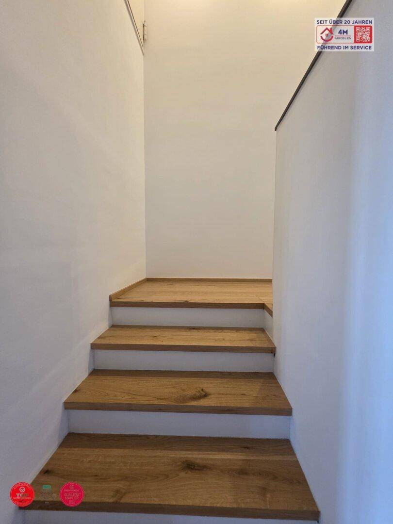 Holztreppe mit weißen Setzstufen, die in die obere Etage führt.