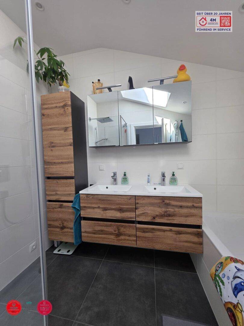 Badezimmer mit Doppelwaschbecken, Holzunterschränken und Dachfenster.