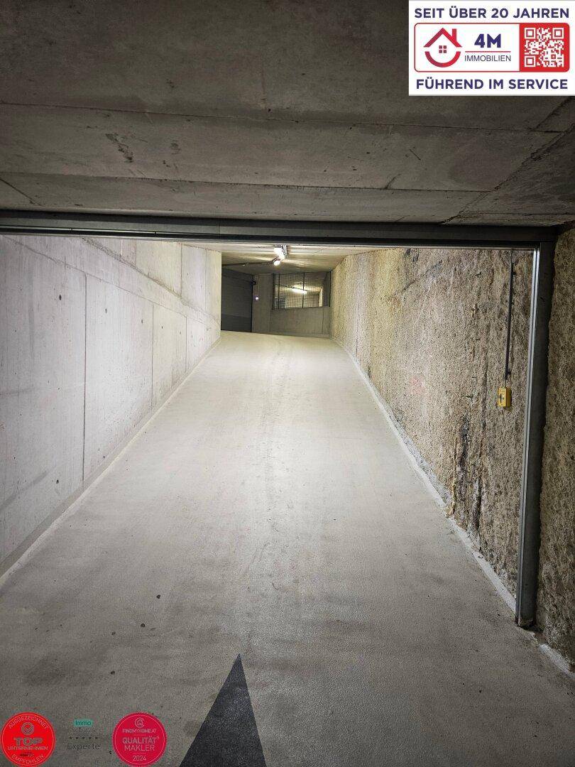 Einfahrtsrampe zur Tiefgarage mit Betonwänden und Beleuchtung.