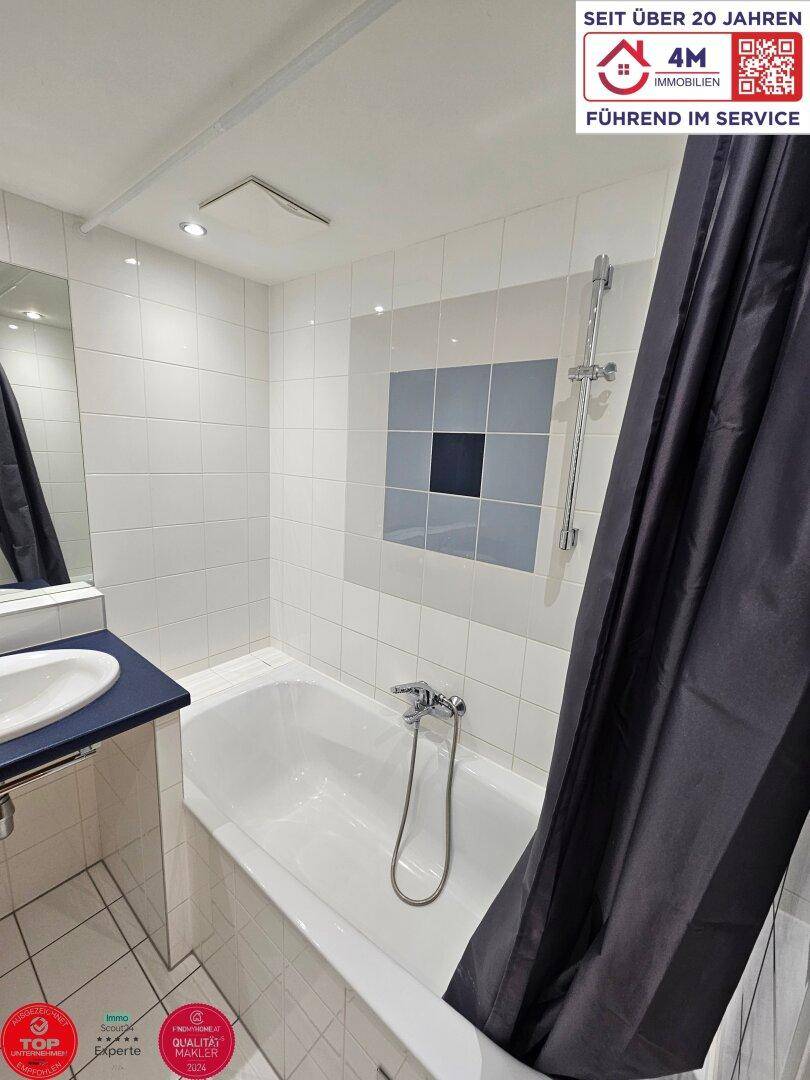 Badezimmer mit Badewanne, Duschvorhang und dekorativen blauen Fliesenakzenten an der Wand.