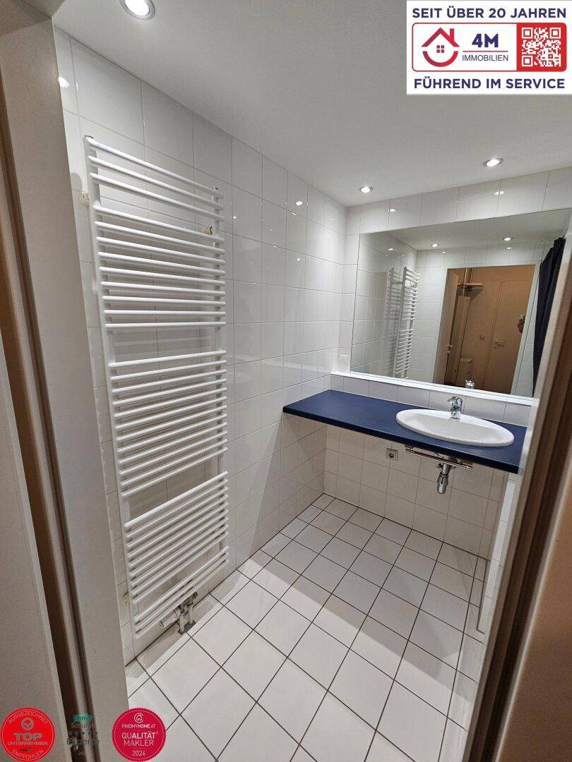 Modernes Badezimmer mit weißen Fliesen, Einzelwaschbecken und beheiztem Handtuchhalter.