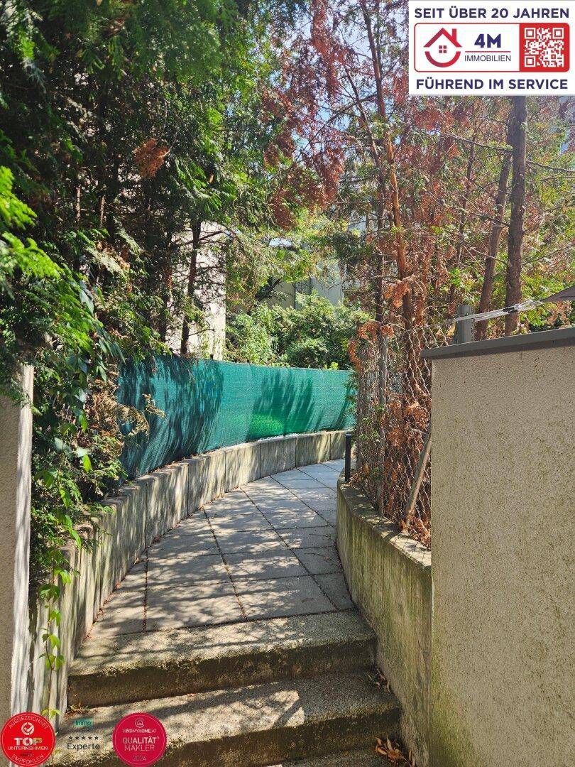 Geschwungener Gartenweg, umgeben von üppigem Grün und Bäumen, der zum Gebäude führt.